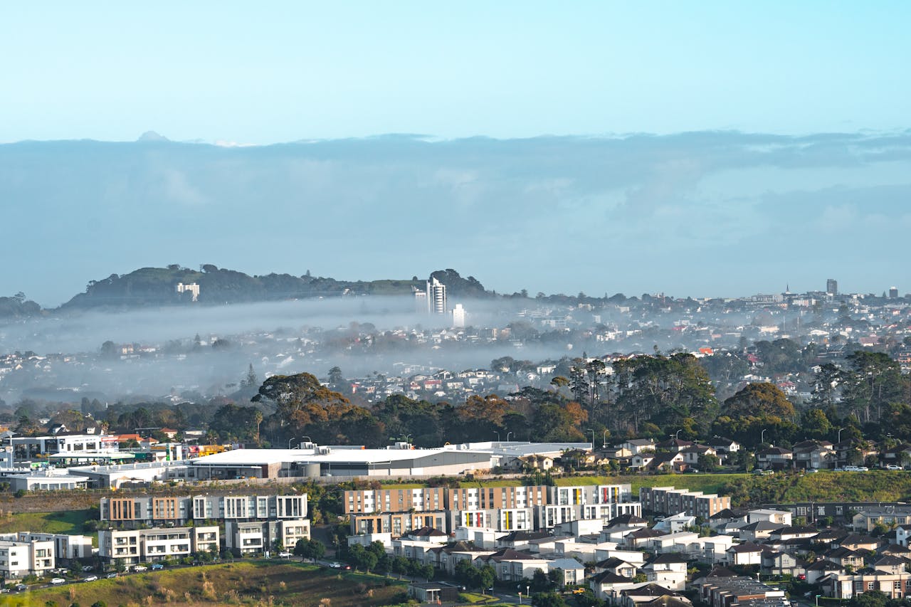 Stunning aerial view of an Auckland suburb blanketed in morning fog, showcasing New Zealand's unique landscape.