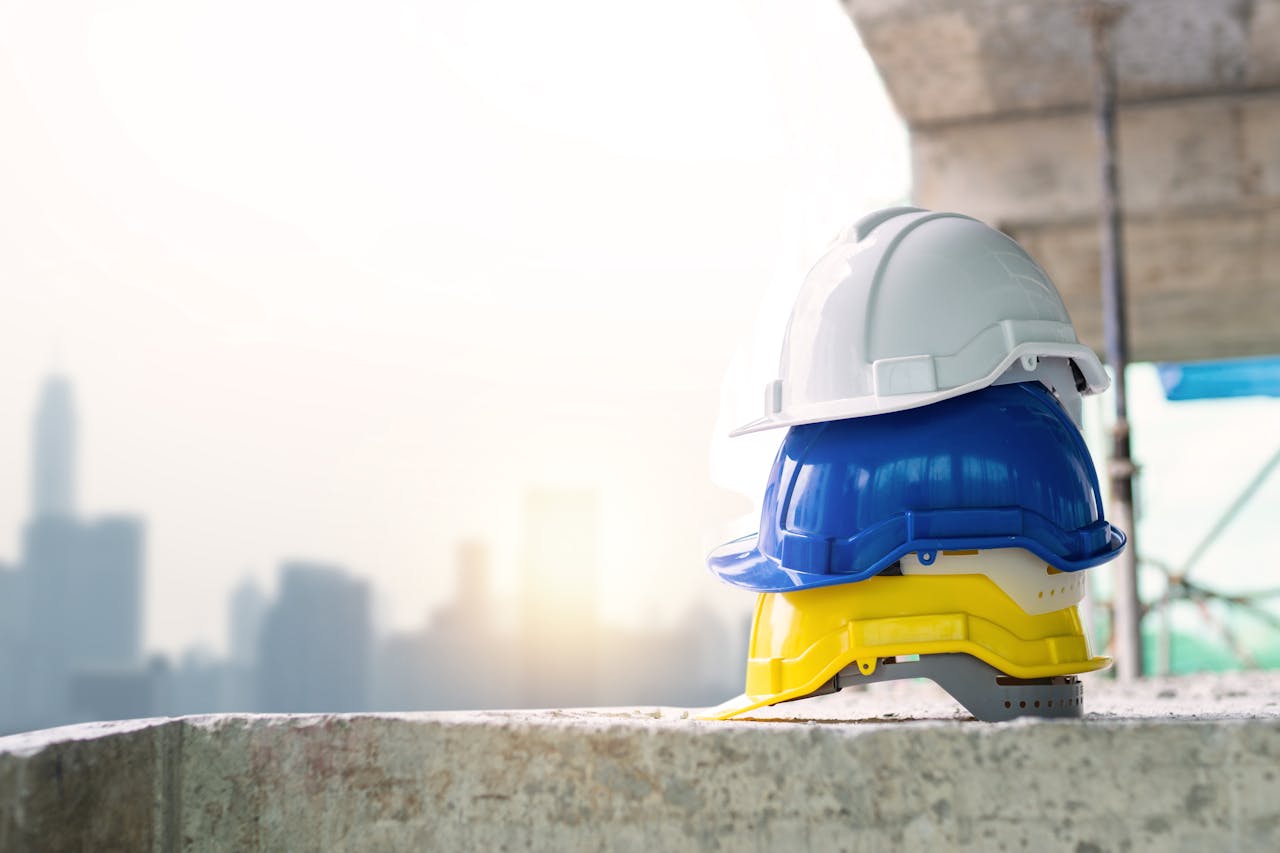 Three colorful safety helmets stacked on a concrete surface with city skyline in background.